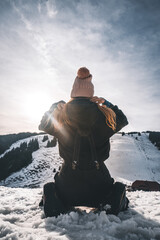 Vertical rear view of a young woman wearing winter hat kneeling down in the snow