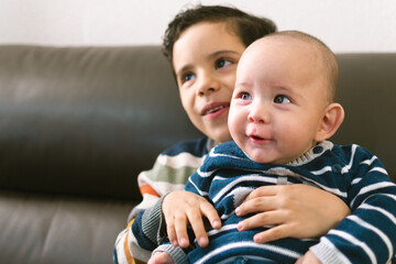 CHILD AND BABY LATIN BROTHERS LAUGHING IN A BROWN COUCH
