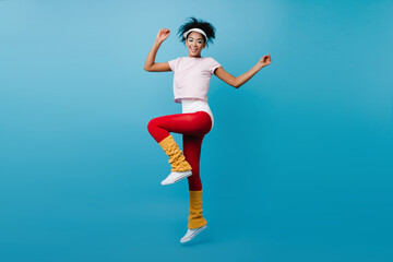Fototapeta na wymiar Graceful black girl doing aerobics. Gorgeous african woman jumping on blue background.