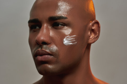 Closeup portrait of handsome young african american man with cream applied on his cheek looking away while posing isolated over gray background