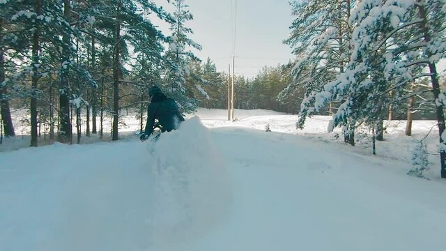 Cyclist in Black Clothes, Helmet and Snow Glasses Riding on Electric Bike in the Snow in Winter Forest. E-Bike Riding and Drifting at Cold Sunny Day - Super Slow Motion