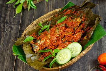 Pepes Ikan Layang or Pais Ikan or Steamed mackerel fish, typically Indonesian traditional food made from fish, spices, wrapped with banana leaves and steamed. Dark Wooden background. 