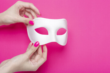 Girl holding white carnival mask and fluffy feather on pink fuchsia background