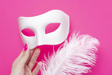 Girl holding white carnival mask and fluffy feather on pink fuchsia background