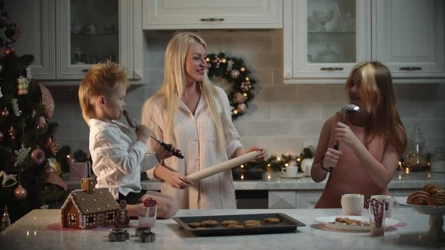 Family christmas - mother and her children having fun in the kitchen - the girl singing in the ladle