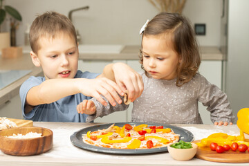 Cute little girl 2-4 in gray dress and boy 7-10 in T-shirt cooking pizza together in kitchen. Brother and sister cooking