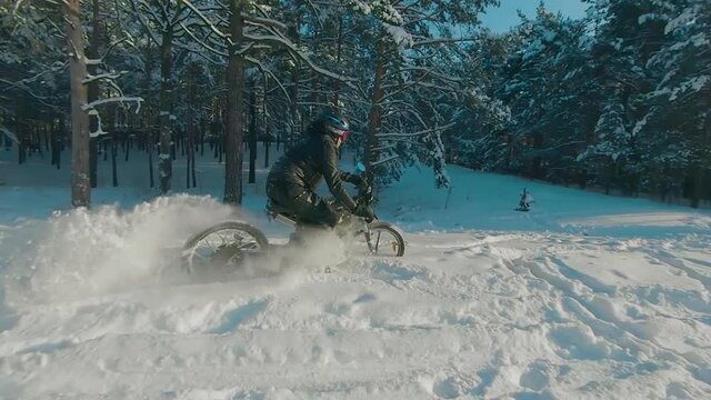 Cyclist in Black Clothes, Helmet and Snow Glasses Riding on Electric Bike in the Snow in Winter Forest. E-Bike Riding and Drifting at Cold Sunny Day - Super Slow Motion