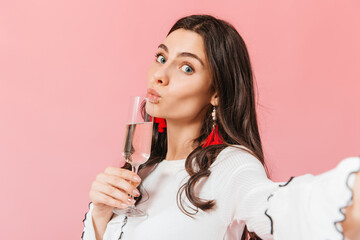 Blue-eyed girl makes selfie on pink background with glass of sparkling wine