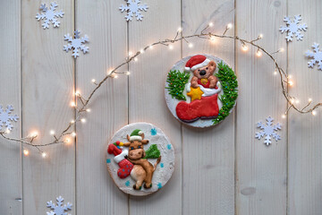 Decorated gingerbread. Cartoon happy cow and bear characters. Creative traditional gifts for children. Christmas flat lay with snowflakes and garland of festive lights. Rustic off white wood table