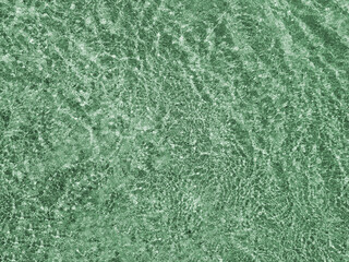 Green ripples of light reflect through shallow water on a sunny day