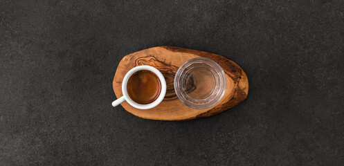 Cup of espresso coffee and glass on wooden pad on dark table, speciality coffee serving concept....