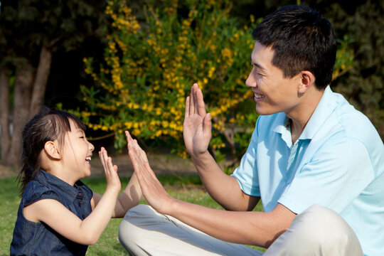 Father and daughter playing clapping games on grass - Powered by Adobe