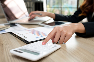 Close up woman hand using calculator and laptop make note with calculate about cost at home office.