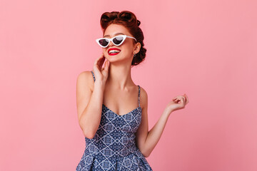 Magnificent pinup girl posing in sunglasses. Studio shot of dreamy ginger woman isolated on pink background.