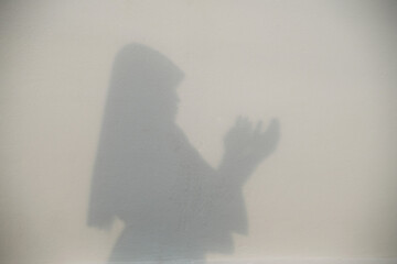 A shadow of a muslim woman praying With a concrete wall background