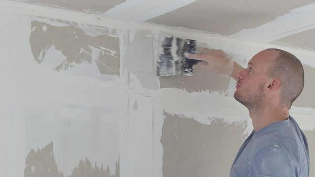 Man plastering wall with putty-knife, close up image. Fixing wall surface and preparation for painting. Putty plaster on the wall. Plastering wall. Craftsman working with plaster. Handyman smoothing