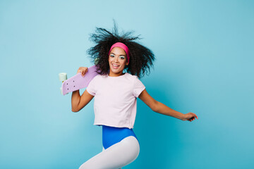 Gorgeous black girl in aerobics form jumping on blue background. Excited curly woman posing with...