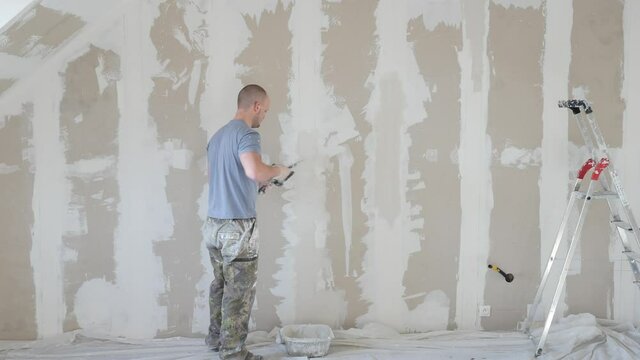Construction worker assemble and patch plaster wall  fixing the drywall to the ceiling metal frame with screwdriver. Renovation, construction and do it yourself DIY concept. Drywall installation,