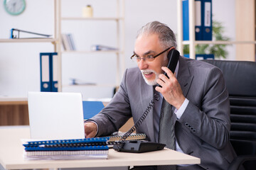 Obraz premium Old male employee using phone in the office