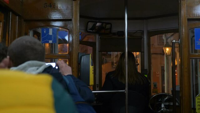 Couple of tourists ride in an old tram along a narrow European street in city center and take pictures of sights and take selfies on their smartphone in evening.