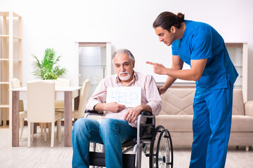 Fototapeta premium Old man in wheel-chair and young bad caregiver indoors