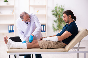 Fototapeta premium Young injured man visiting old doctor traumatologist