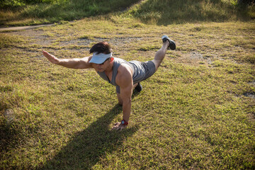 A fit and youthful asian man performs bird dogs on the grass of an open field. Lower back and ab workout.