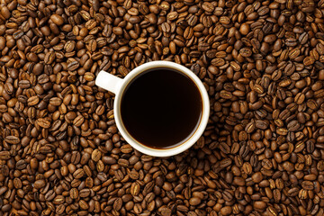 top view of fresh roasted coffee beans with a cup full of coffee in the center, background