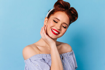 Pleasant ginger lady posing with sincere smile. Studio shot of blissful pinup female model isolated on blue background.