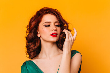 Pleasant female model posing on yellow background. Studio shot of romantic ginger girl in green dress.