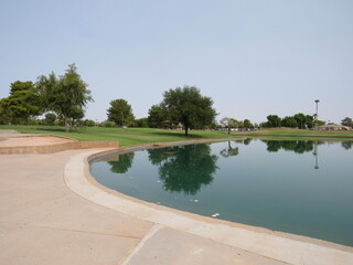 A park with a large man-made water reservoir and a golf course in the distance with people practicing located in Arizona