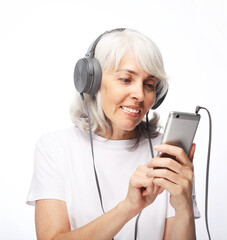 Old people, emotion and technology concept: portrait of happy senior woman with white hair listening to music with headphones over white background