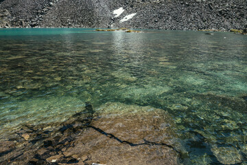 Beautiful nature background of stony bottom in turquoise transparent water of glacial lake in sunlight. Sunny backdrop with many stones in green clear water of glacier lake. Texture of mountain lake.