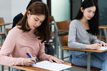 Fototapeta premium Young female university students concentrate on doing examinations in the classroom. Girl students seriously write the exercise of the examinations in the classroom.