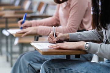 Young female university students concentrate on doing examinations in the classroom. Girl students seriously write the exercise of the examinations in the classroom.