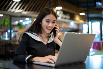 Asian woman using computer notebook and talking on the phone about working at the office.