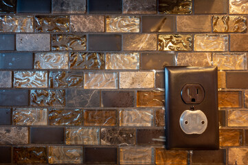Dark electrical outlet against a tiled kitchen back splash with plastic inserts to prevent a child or baby from getting shocked