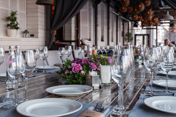 Modern veranda restaurant interior, flowers, banquet setting, glasses, plates