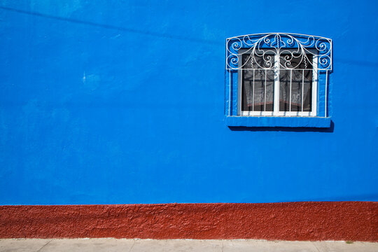 A window covered with an ornate iron cover in a blue wall with brick texture at the bottom.