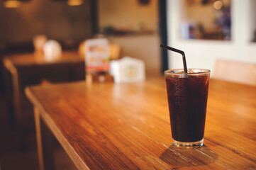 Iced black coffee in a glass is on a wooden table.