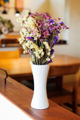 A bouquet of dried flowers in a tall white flower vase