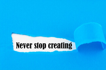 Text Never stop creating appearing behind torn blue paper