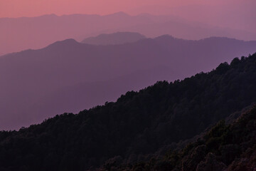 View of Himalayas mountain range with visible silhouettes through the colorful fog from Binsar Zero point trek trail in  himalayan region of Kumaon, Uttarakhand, India.