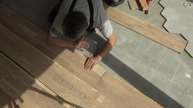Male worker lay oak floor boards. New apartment finishing works. Static closeup shot.