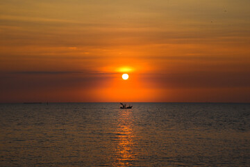 A beautiful sunset in the evening A fisherman's boat passed at Bang Saen Beach, Thailand.