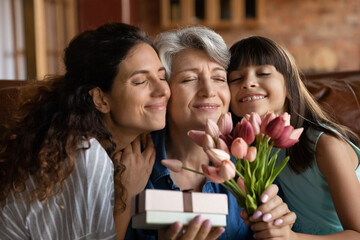 Close up happy three generations of women celebrating event, touching cheeks, cute little girl with...