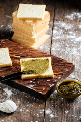 Side view on spreading white bread slice with pesto sauce on the wooden cutting board