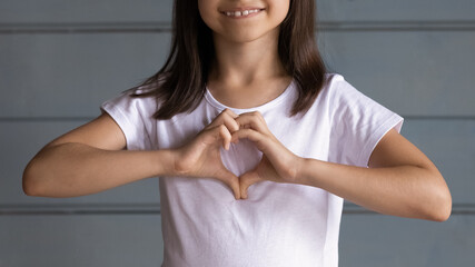 Close up smiling adorable little girl showing heart gesture, happy cute preschool child kid wearing...