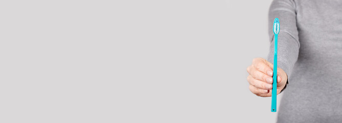 Hand with blue toothbrush on grey background.