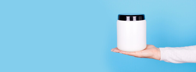 Hand with white cosmetic bottle on blue background.